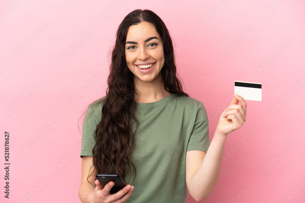 Young caucasian woman isolated on pink background buying with the mobile with a credit card Young caucasian woman isolated on pink background buying with the mobile with a credit card