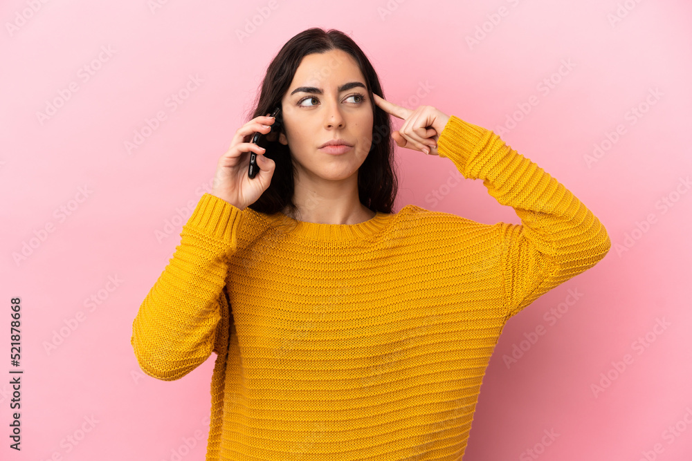 Young caucasian woman using mobile phone isolated on pink background having doubts and thinking Young caucasian woman using mobile phone isolated on pink background having doubts and thinking