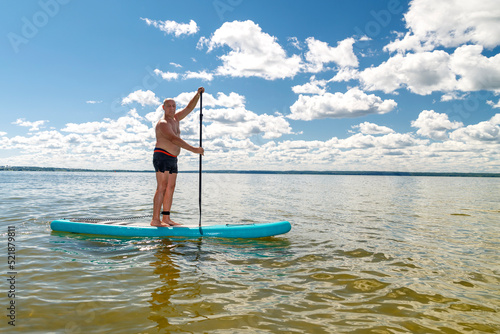 A man in shorts on a SUP board with an oar floats standing on the water against the blue sky.