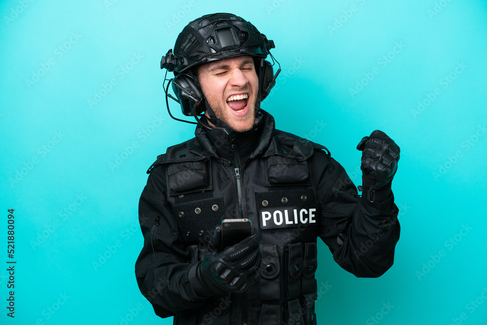 SWAT caucasian man isolated on blue background with phone in victory position SWAT caucasian man isolated on blue background with phone in victory position