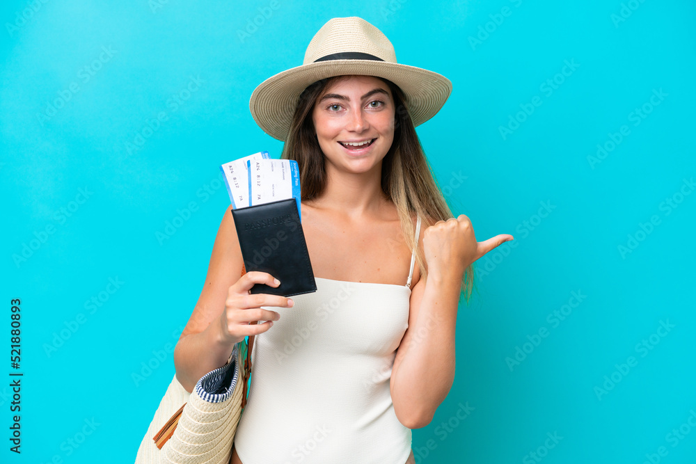 Young woman in swimsuit holding passport isolated on blue background pointing to the side to present a product Young woman in swimsuit holding passport isolated on blue background pointing to the side to present a product