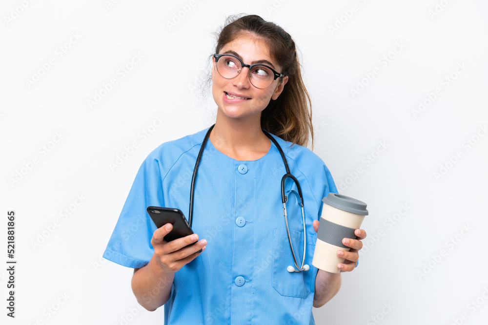 Young nurse doctor woman isolated on white background holding coffee to take away and a mobile while thinking something Young nurse doctor woman isolated on white background holding coffee to take away and a mobile while thinking something