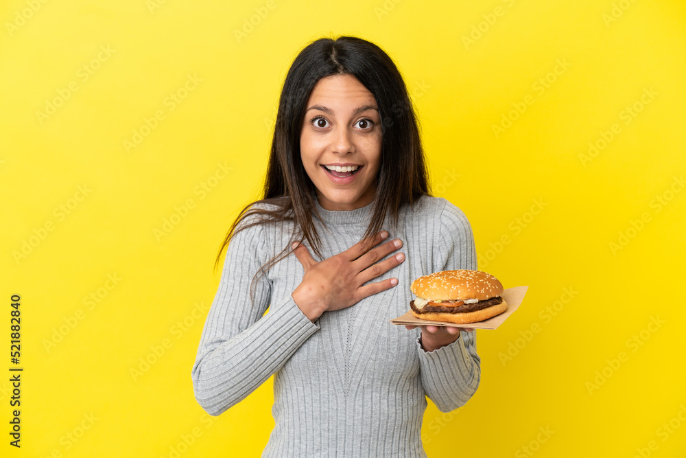 Young caucasian woman holding a burger isolated on yellow background surprised and shocked while looking right Young caucasian woman holding a burger isolated on yellow background surprised and shocked while looking right