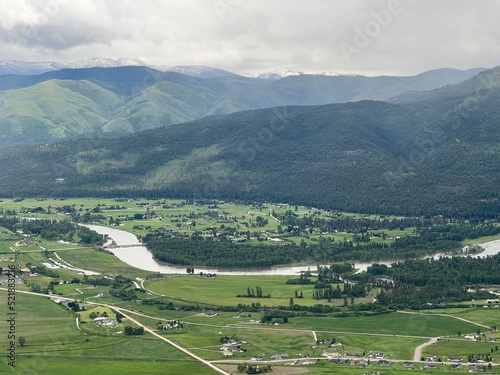 Aerial view of the Bitterroot River flowing through lush, green fields, next to homes, hills and mountains in Missoula area, Montana, USA. Rain clouds overhead photo
