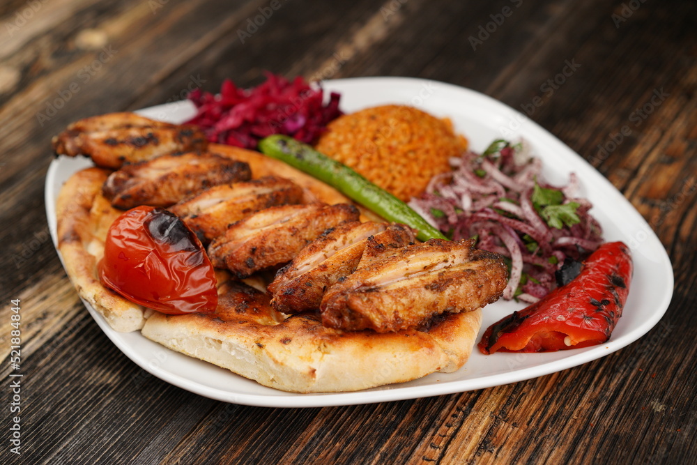 Grilled Turkish chicken wings served with pita, garnish, onions, bulgur, roasted green pepper, and roasted tomato on a white plate on wooden background. Served special restaurant presentation Grilled Turkish chicken wings served with pita, garnish, onions, bulgur, roasted green pepper, and roasted tomato on a white plate on wooden background. Served special restaurant presentation