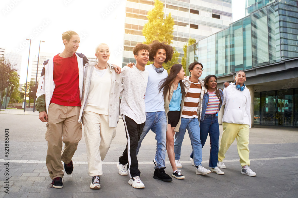 Smiling multiracial young people walking and hugging in the city. Group of happy teenagers friends having fun together outdoors.