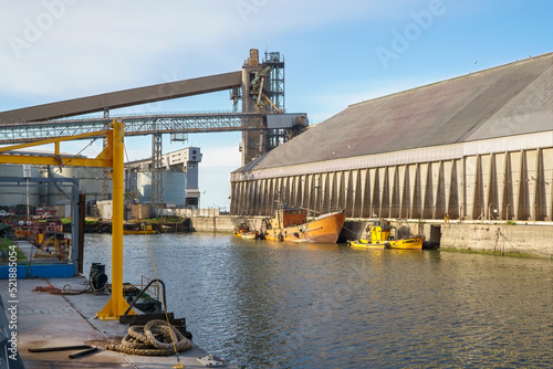 Maritime harbor with grain loading dock, shed and silos. Some small fishing boats around