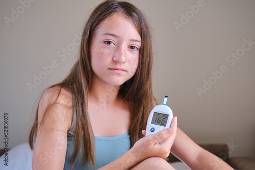A teenage girl shows the screen of a glucometer with the results of a blood test for diabetes into the camera.