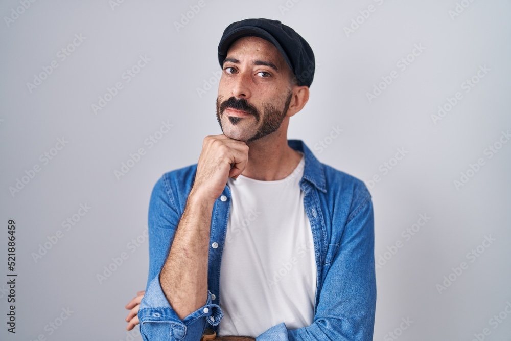 Hispanic man with beard standing over isolated background with hand on chin thinking about question, pensive expression. smiling with thoughtful face. doubt concept. Hispanic man with beard standing over isolated background with hand on chin thinking about question, pensive expression. smiling with thoughtful face. doubt concept.