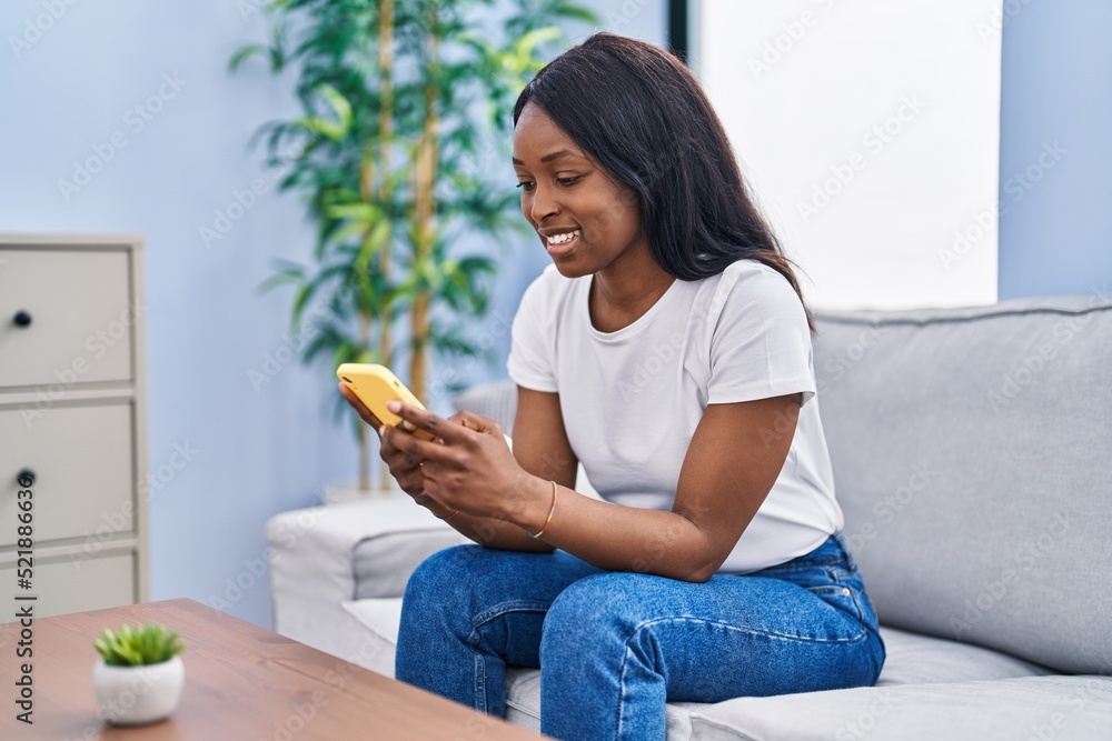 Young african american woman using smartphone sitting on sofa at home Young african american woman using smartphone sitting on sofa at home