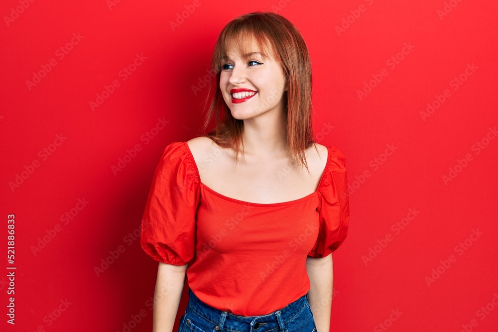 Redhead young woman wearing casual red t shirt looking away to side with smile on face, natural expression. laughing confident. Redhead young woman wearing casual red t shirt looking away to side with smile on face, natural expression. laughing confident.