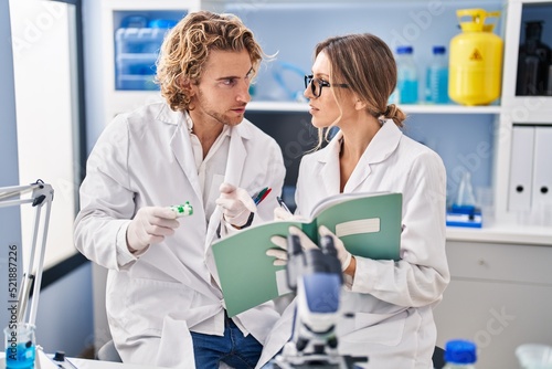 Man and woman wearing scientist uniform holding pills writing on notebook at laboratory