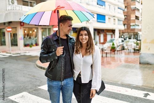 Young couple smiling happy holding umbrella standing at the city. © Krakenimages.com