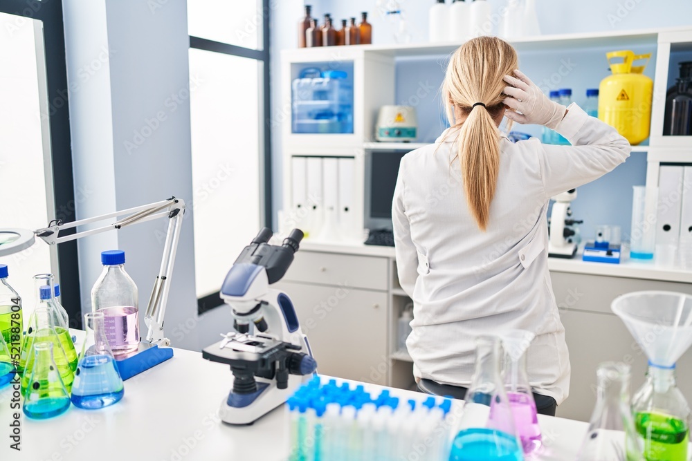 Middle age blonde woman working at scientist laboratory backwards thinking about doubt with hand on head Middle age blonde woman working at scientist laboratory backwards thinking about doubt with hand on head