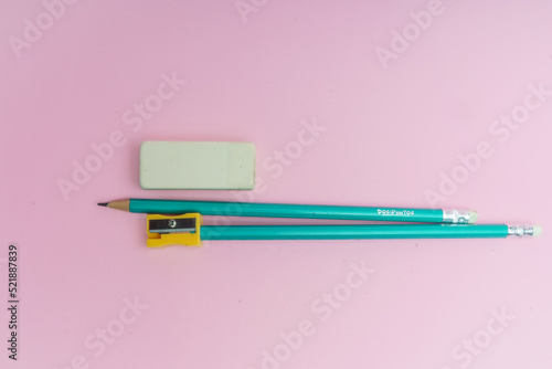 Lápices azules, borrador blanco y sacapuntas amarillo sobre fondo rosa. photo