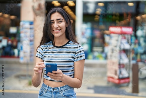 Young hispanic girl smiling confident using smartphone at street