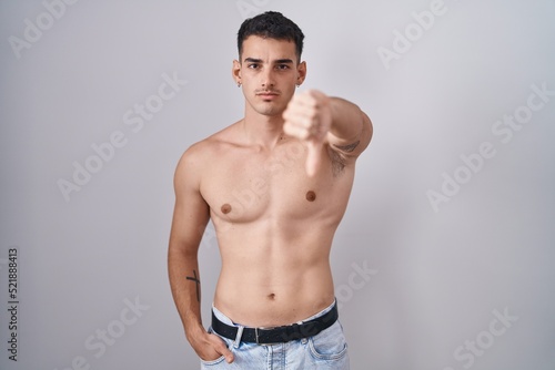 Handsome hispanic man standing shirtless looking unhappy and angry showing rejection and negative with thumbs down gesture. bad expression.