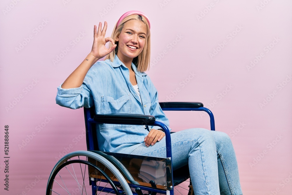 Beautiful blonde woman sitting on wheelchair smiling positive doing ok sign with hand and fingers. successful expression. Beautiful blonde woman sitting on wheelchair smiling positive doing ok sign with hand and fingers. successful expression.