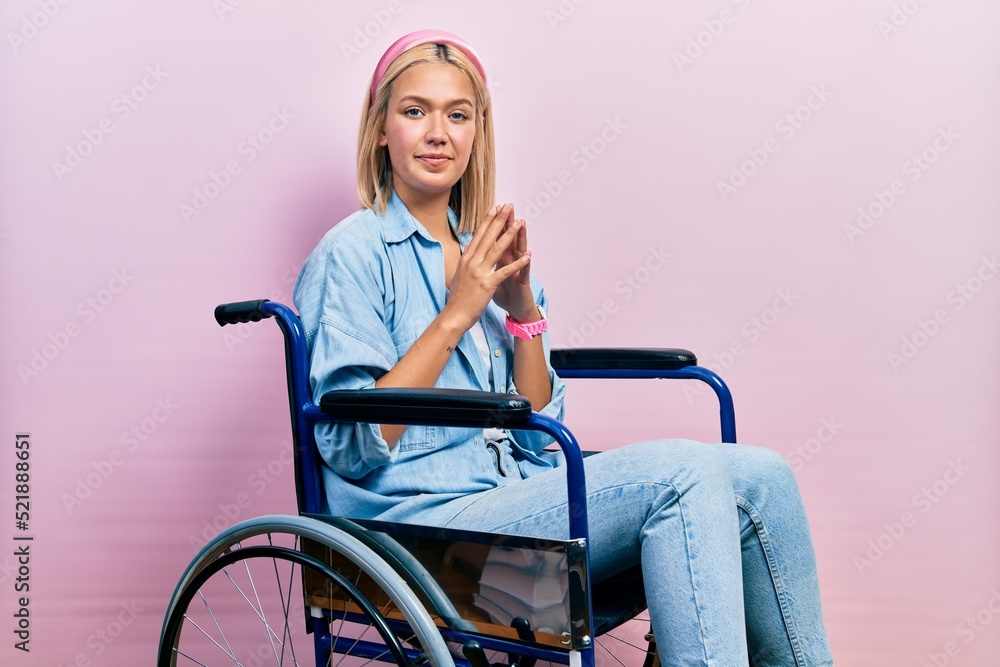 Beautiful blonde woman sitting on wheelchair hands together and fingers crossed smiling relaxed and cheerful. success and optimistic Beautiful blonde woman sitting on wheelchair hands together and fingers crossed smiling relaxed and cheerful. success and optimistic