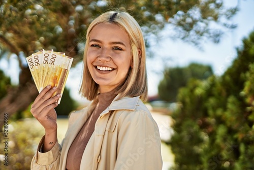 Young blonde girl smiling happy holding norway krone banknotes at the city.