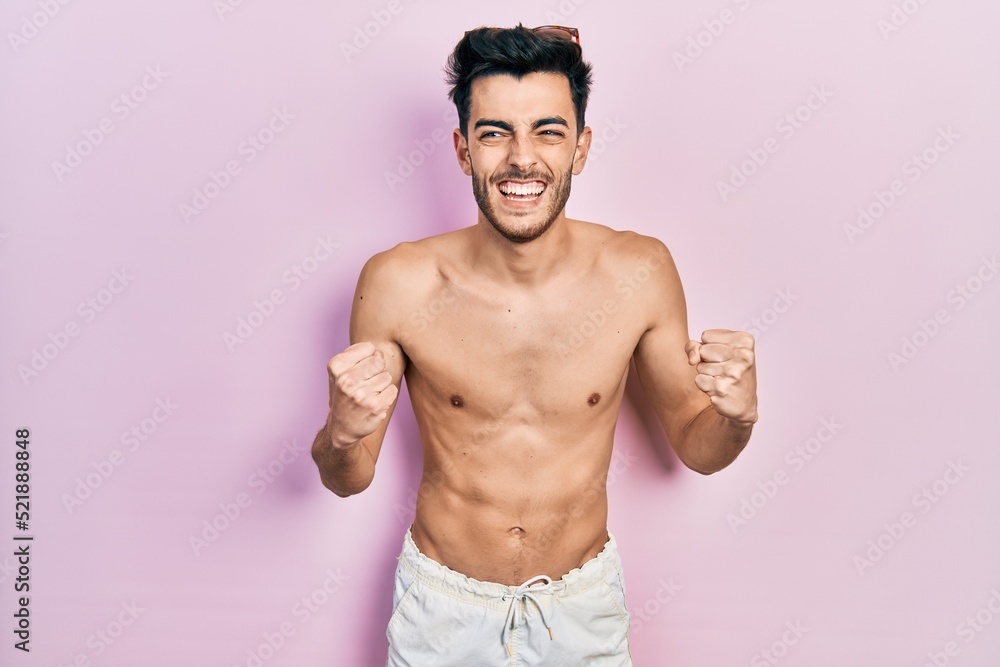 Young hispanic man wearing swimwear shirtless very happy and excited doing winner gesture with arms raised, smiling and screaming for success. celebration concept.