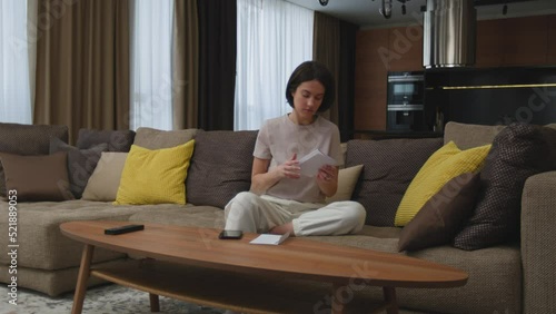 Upset female tenant homeowner looking through apartment bills sitting in living room at home, check financial taxes fees