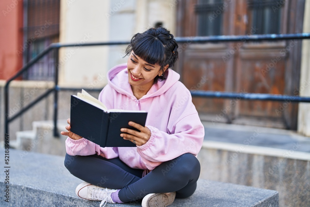 Young woman reading book sitting on bench at street Young woman reading book sitting on bench at street