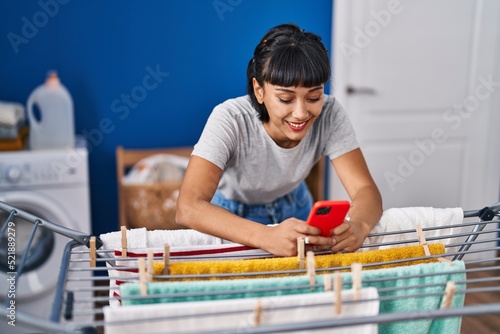 Young woman using smartphone hanging clothes at laundry room