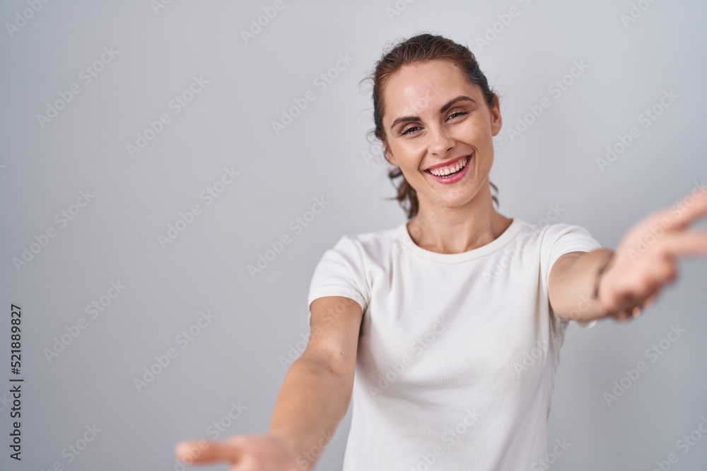 Beautiful brunette woman standing over isolated background looking at the camera smiling with open arms for hug. cheerful expression embracing happiness. Beautiful brunette woman standing over isolated background looking at the camera smiling with open arms for hug. cheerful expression embracing happiness.