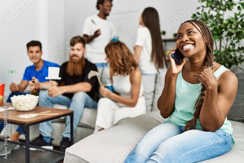 Group of young friends smiling happy sitting on the sofa. Woman using smartphone at home.