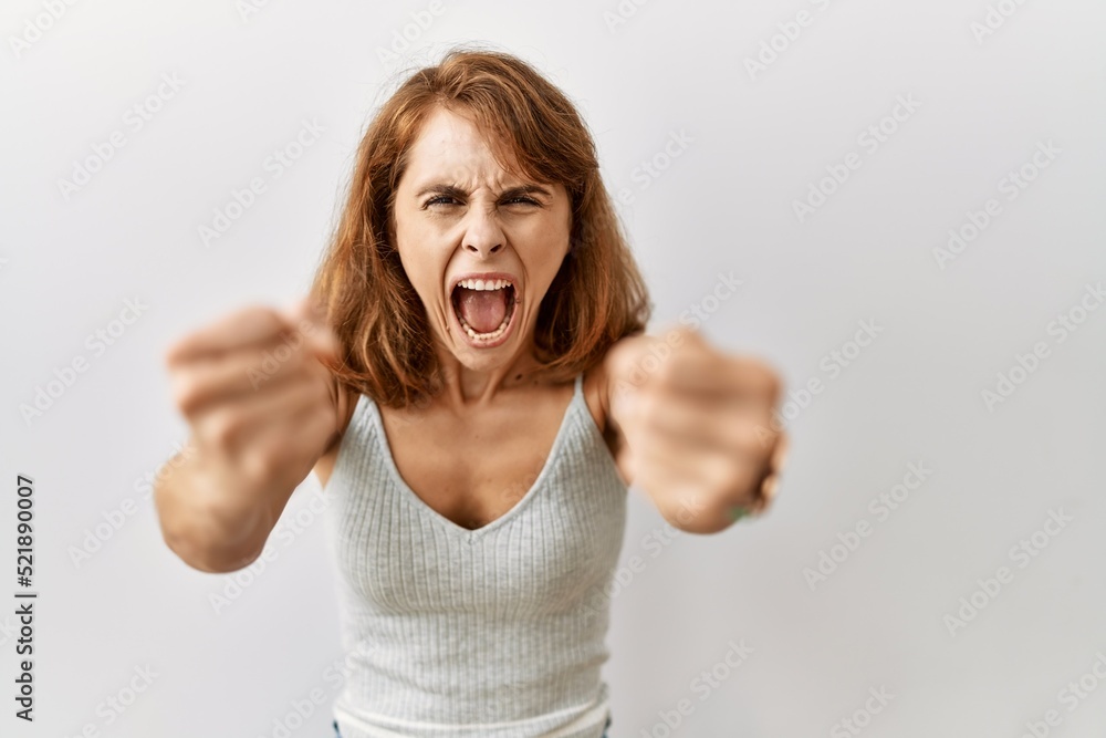 Beautiful caucasian woman standing over isolated background angry and mad raising fists frustrated and furious while shouting with anger. rage and aggressive concept. Beautiful caucasian woman standing over isolated background angry and mad raising fists frustrated and furious while shouting with anger. rage and aggressive concept.