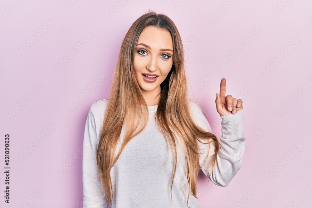 Young blonde girl wearing casual clothes smiling with an idea or question pointing finger up with happy face, number one Young blonde girl wearing casual clothes smiling with an idea or question pointing finger up with happy face, number one