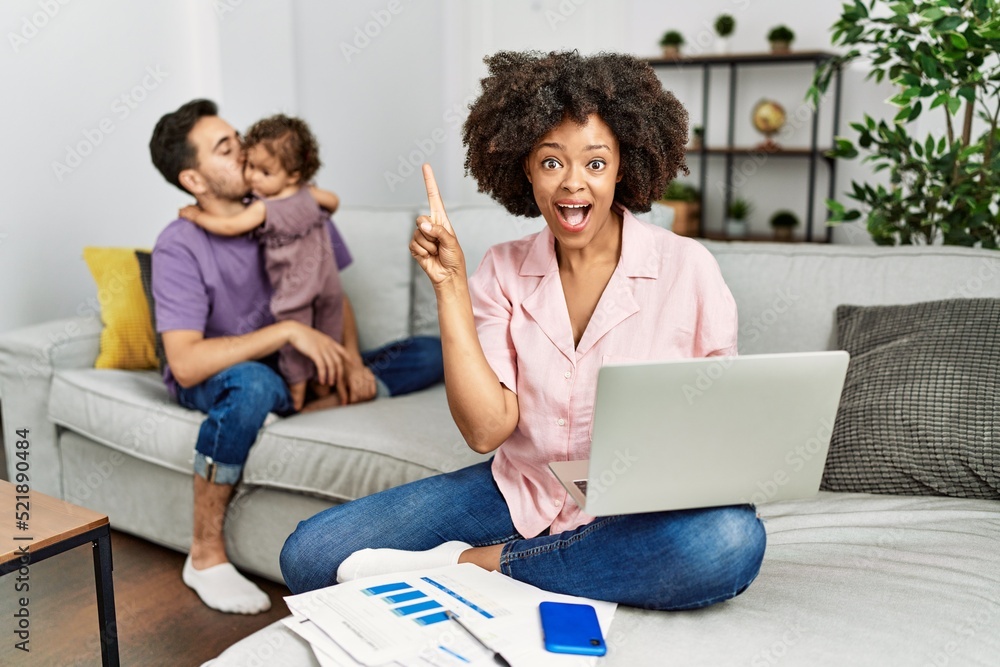 Mother of interracial family working using computer laptop at home pointing finger up with successful idea. exited and happy. number one. Mother of interracial family working using computer laptop at home pointing finger up with successful idea. exited and happy. number one.