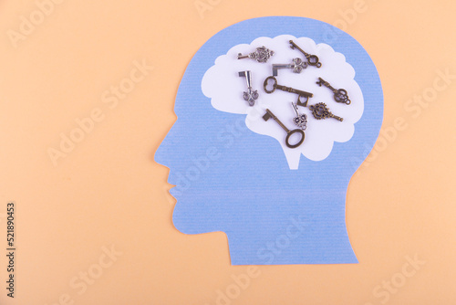 Top view on creative thinking man with various keys in brain. Paper face on light beige background. Copy space for text