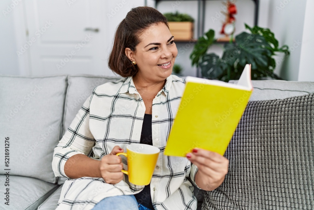 Middle age hispanic woman reading book drinking coffee at home Middle age hispanic woman reading book drinking coffee at home