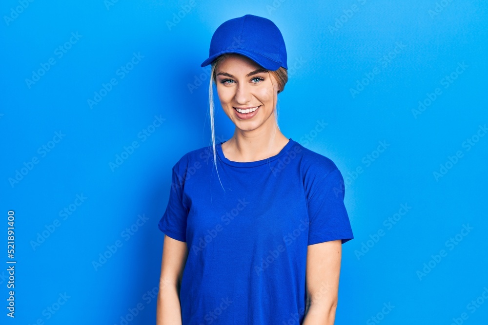 Young caucasian woman wearing courier uniform wearing cap looking positive and happy standing and smiling with a confident smile showing teeth Young caucasian woman wearing courier uniform wearing cap looking positive and happy standing and smiling with a confident smile showing teeth