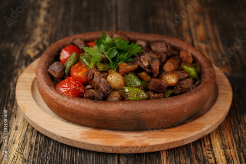 Title: Saute meat in a stew on a wooden background. Meat saute made with beef, mushroom, onion, green pepper and tomatoes. A delicious traditional Turkish food name is Guvec.