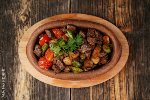 Title: Saute meat in a stew on a wooden background. Meat saute made with beef, mushroom, onion, green pepper and tomatoes. A delicious traditional Turkish food name is Guvec.
