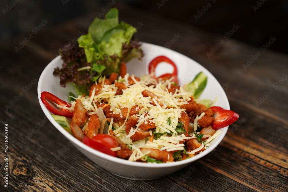 Salad with fried chicken. Salad made with fried chicken, tomatoes, cucumber, green pepper, and grated cheese in a white bowl. Delicious health food. Salad with fried chicken. Salad made with fried chicken, tomatoes, cucumber, green pepper, and grated cheese in a white bowl. Delicious health food.