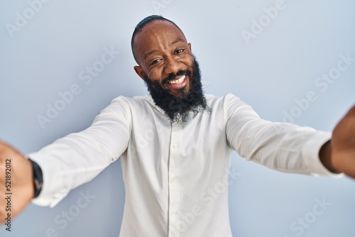 African american man standing over blue background looking at the camera smiling with open arms for hug. cheerful expression embracing happiness.