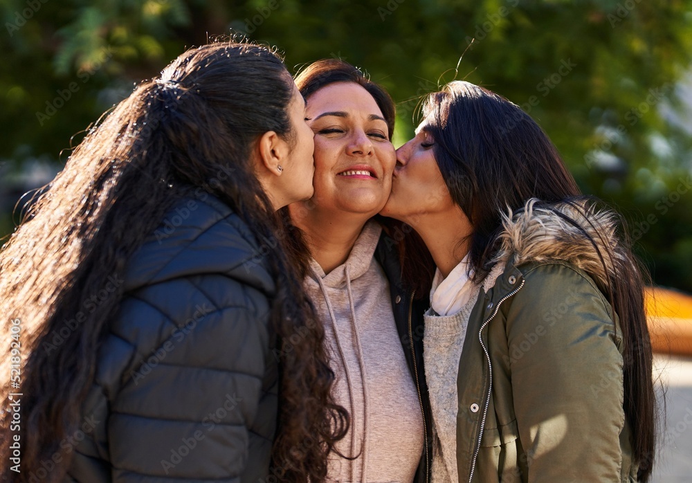 Fototapeta premium Three woman mother and daughters standing together and kissing at park