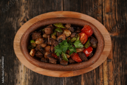 Saute meat in a stew on a wood background. Meat saute made with beef, mushroom, onion, green pepper and tomatoes. A delicious traditional Turkish food name is Guvec. Top view.