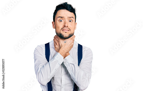 Hispanic man with beard wearing hipster look with bow tie and suspenders shouting and suffocate because painful strangle. health problem. asphyxiate and suicide concept.