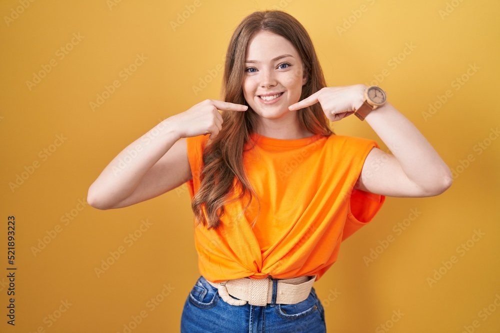 Caucasian woman standing over yellow background smiling cheerful showing and pointing with fingers teeth and mouth. dental health concept. Caucasian woman standing over yellow background smiling cheerful showing and pointing with fingers teeth and mouth. dental health concept.
