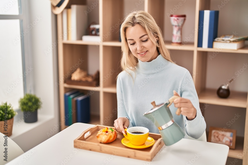 Young blonde woman having breakfast sitting on table at home