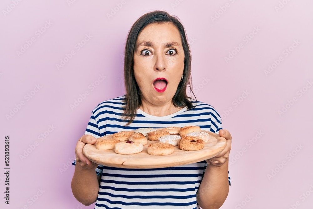 Middle age hispanic woman holding sweet pastries afraid and shocked with surprise and amazed expression, fear and excited face. Middle age hispanic woman holding sweet pastries afraid and shocked with surprise and amazed expression, fear and excited face.