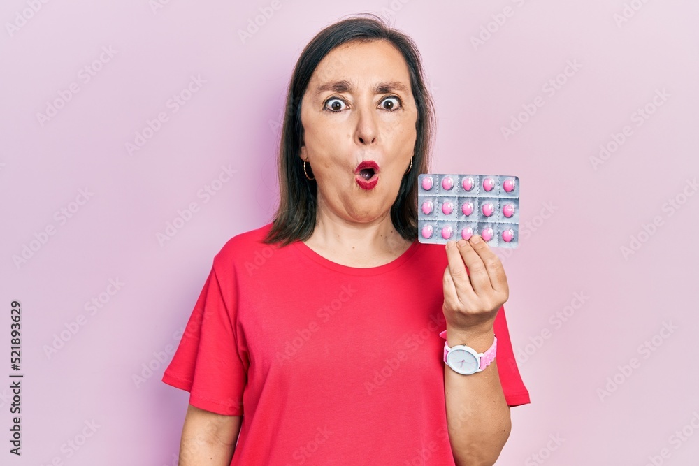 Middle age hispanic woman holding pills scared and amazed with open mouth for surprise, disbelief face Middle age hispanic woman holding pills scared and amazed with open mouth for surprise, disbelief face