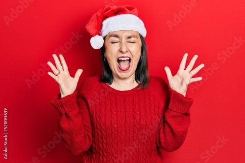 Middle age hispanic woman wearing christmas hat celebrating mad and crazy for success with arms raised and closed eyes screaming excited. winner concept © Krakenimages.com