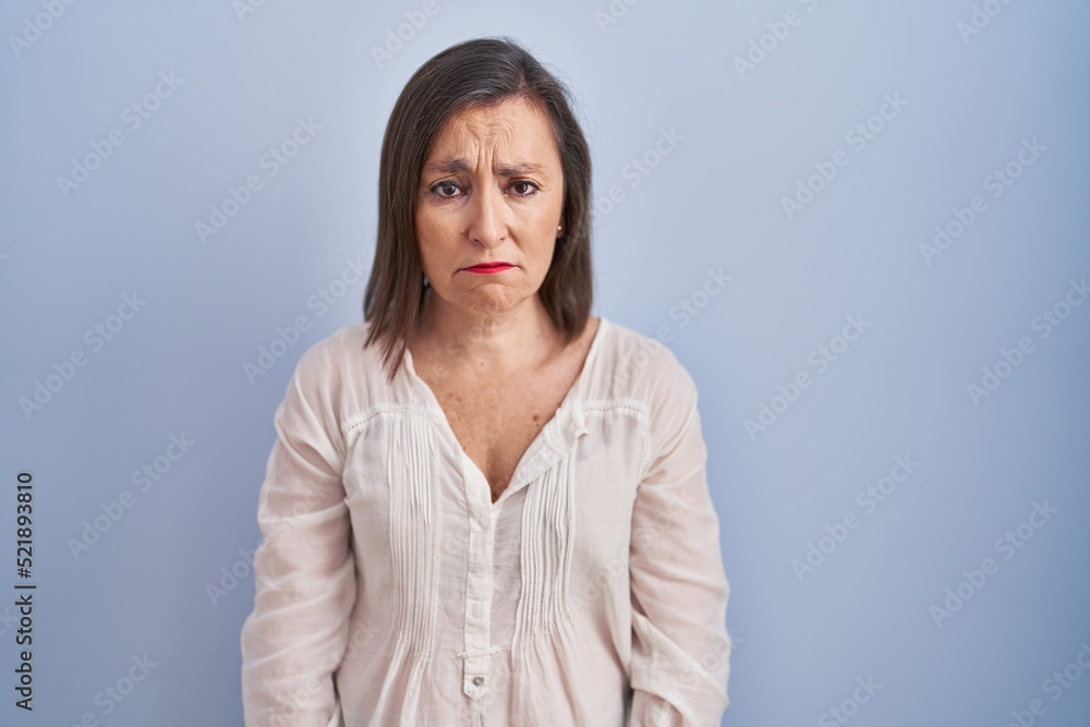 Middle age hispanic woman standing over blue background depressed and worry for distress, crying angry and afraid. sad expression. Middle age hispanic woman standing over blue background depressed and worry for distress, crying angry and afraid. sad expression.
