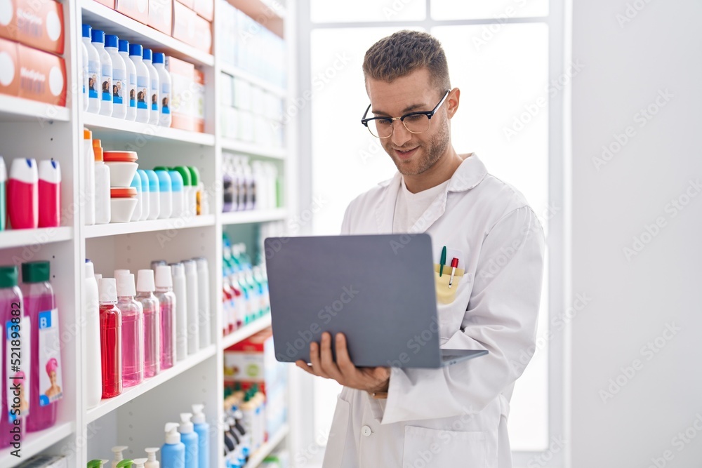 Young caucasian man pharmacist using laptop working at pharmacy